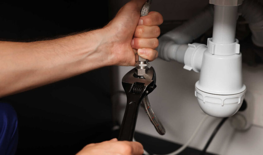 Professional plumber with adjustable wrench fixing sink, closeup
