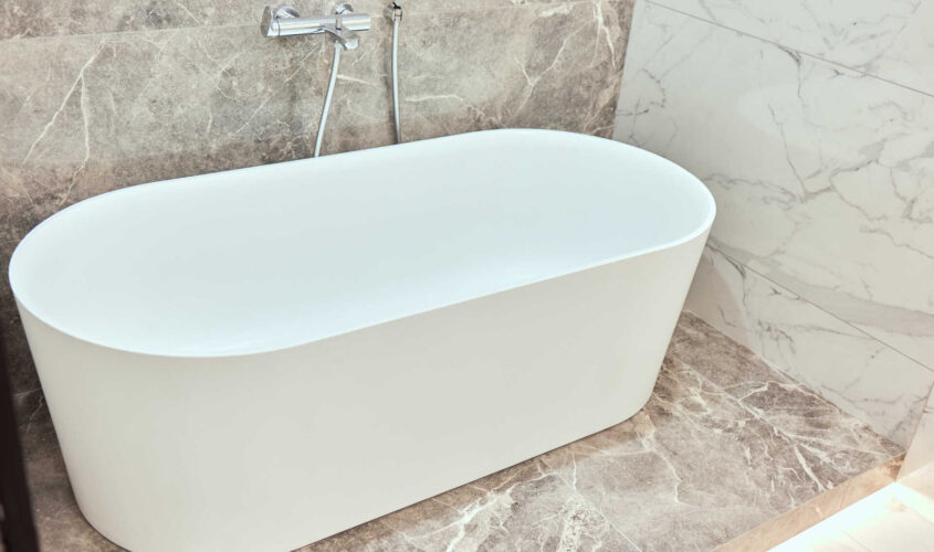 Luxury big oval bathtub in bathroom with black and white marble tiles on walls and floor.
