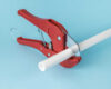 Red Pipe Cutter Tool Cutting White PVC Pipe Against Blue Background