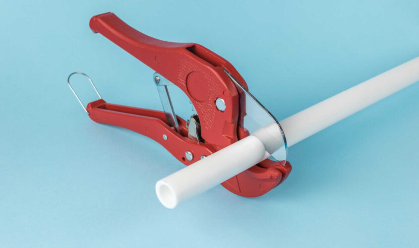 Red Pipe Cutter Tool Cutting White PVC Pipe Against Blue Background
