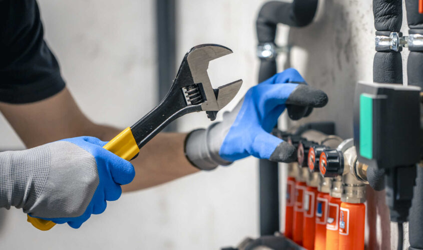 A man installs a heating system in a house and checks the pipes with a wrench.