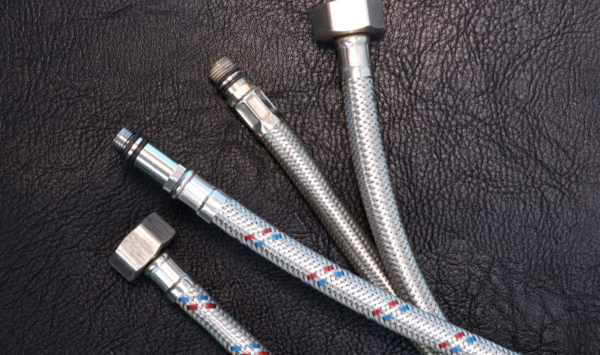 Flexible water hoses in a metal spout for connecting plumbing equipment. Black textured leather background. Copy space for text.